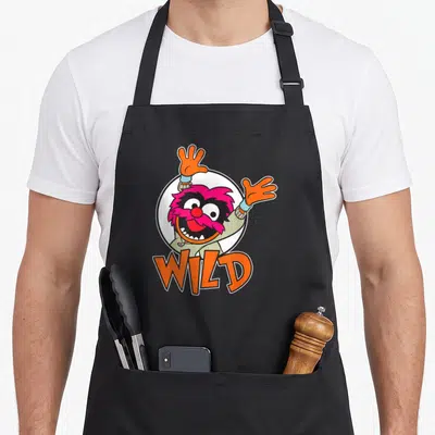 Baby animal apron - Pink cartoon creature with raised orange hands inside white circle, WILD text below — shown on a black cotton canvas apron against a white background