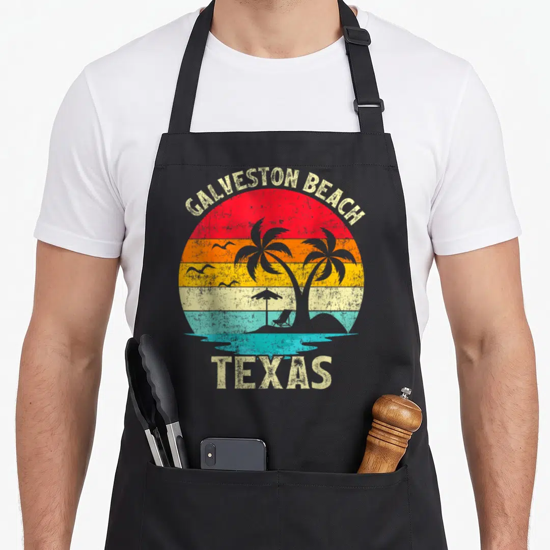 Family vacation texas apron - Retro Galveston Beach Texas sunset with palm tree, beach chair, umbrella, and seagull — shown on a black cotton canvas apron against a white background