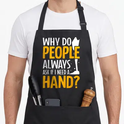 Limb leg apron - Stacked white and yellow text reading Why Do People Always Ask If I Need A Hand next to a white arm — shown on a black cotton canvas apron against a white background
