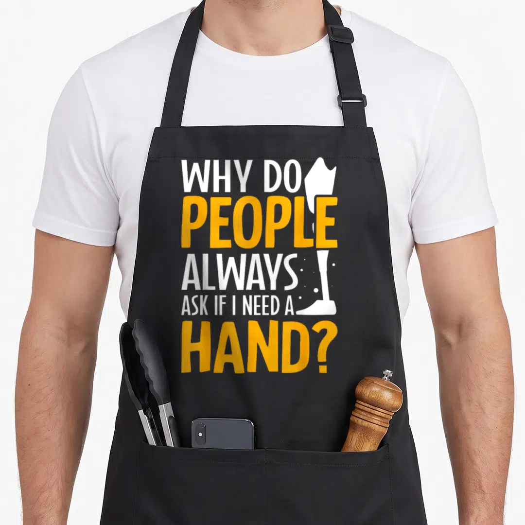 Limb leg apron - Stacked white and yellow text reading Why Do People Always Ask If I Need A Hand next to a white arm — shown on a black cotton canvas apron against a white background