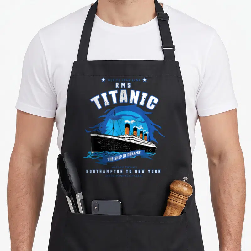 Star line apron - Retro White Star Line Titanic ship print with maiden voyage stats and orange funnels on blue — shown on a black cotton canvas apron against a white background