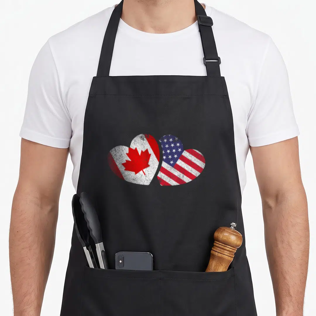 Friendship canada aprons - Two overlapping hearts filled with distressed red white and blue Canadian and American flag — shown on a black cotton canvas apron against a white background