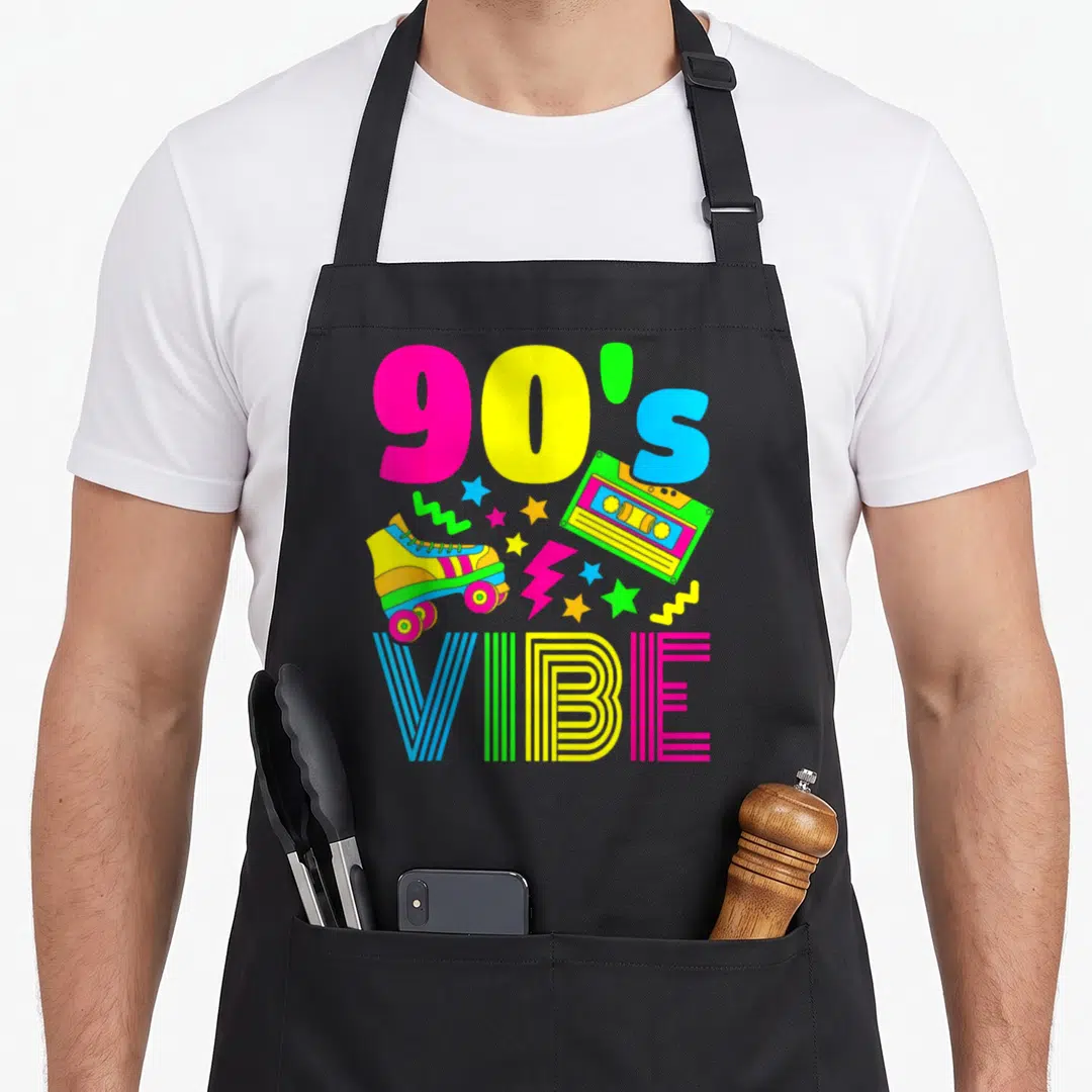 Outfit theme aprons - 90s VIBE text with roller skate, cassette, stars, lightning bolt, zigzags in pink yellow blue — shown on a black cotton canvas apron against a white background