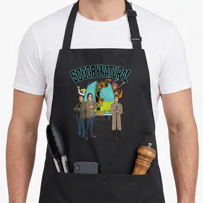 Scoobynatural mystery apron - Arched SCOOBYNATURAL text over characters and Mystery Machine van in teal yellow brown — shown on a black cotton canvas apron against a white background