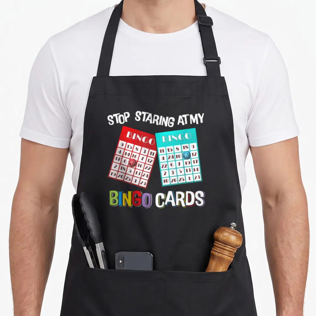 Queen bingo aprons - Arched text Stop Staring At My Bingo Cards over red and blue overlapping bingo cards — shown on a black cotton canvas apron against a white background