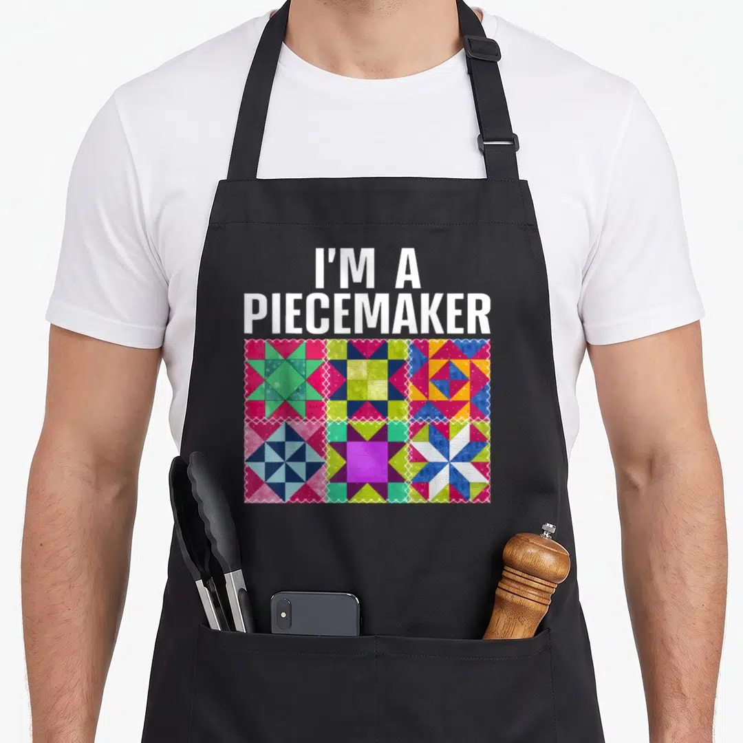 Quilting sewer quilter apron - I'M A PIECEMAKER text above six colorful quilt star blocks in red blue green yellow — shown on a black cotton canvas apron against a white background