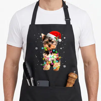 Dog christmas tree apron - Photo of a brown dog in a red Santa hat wrapped in multicolored Christmas lights surrounded — shown on a black cotton canvas apron against a white background