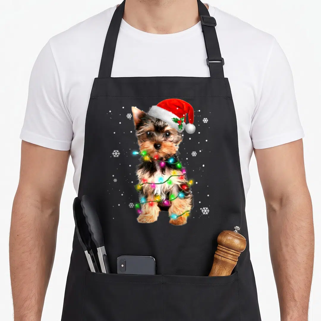 Dog christmas tree apron - Photo of a brown dog in a red Santa hat wrapped in multicolored Christmas lights surrounded — shown on a black cotton canvas apron against a white background