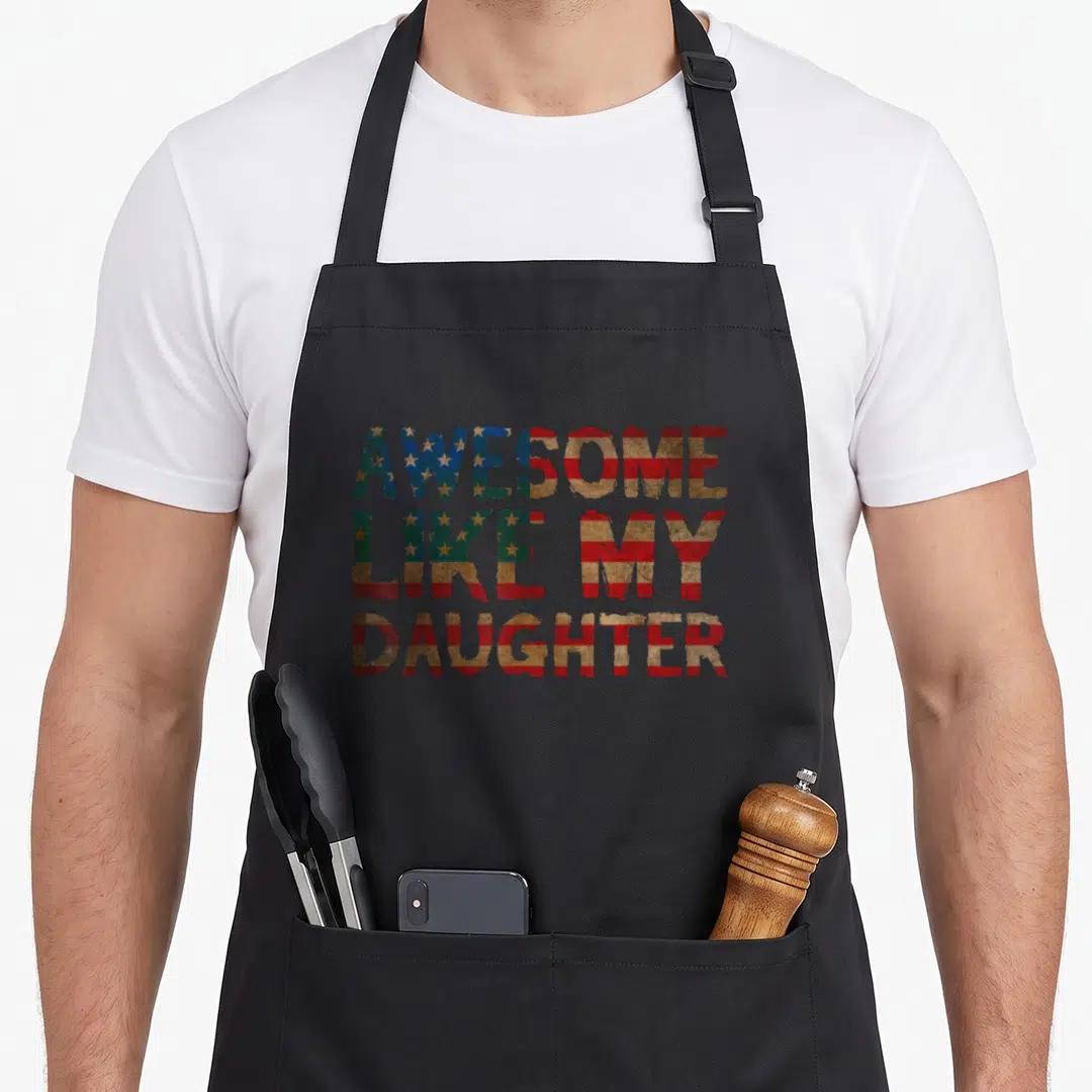4th july father day apron - Distressed text reading Awesome Like My Daughter in patriotic flag colors — shown on a black cotton canvas apron against a white background