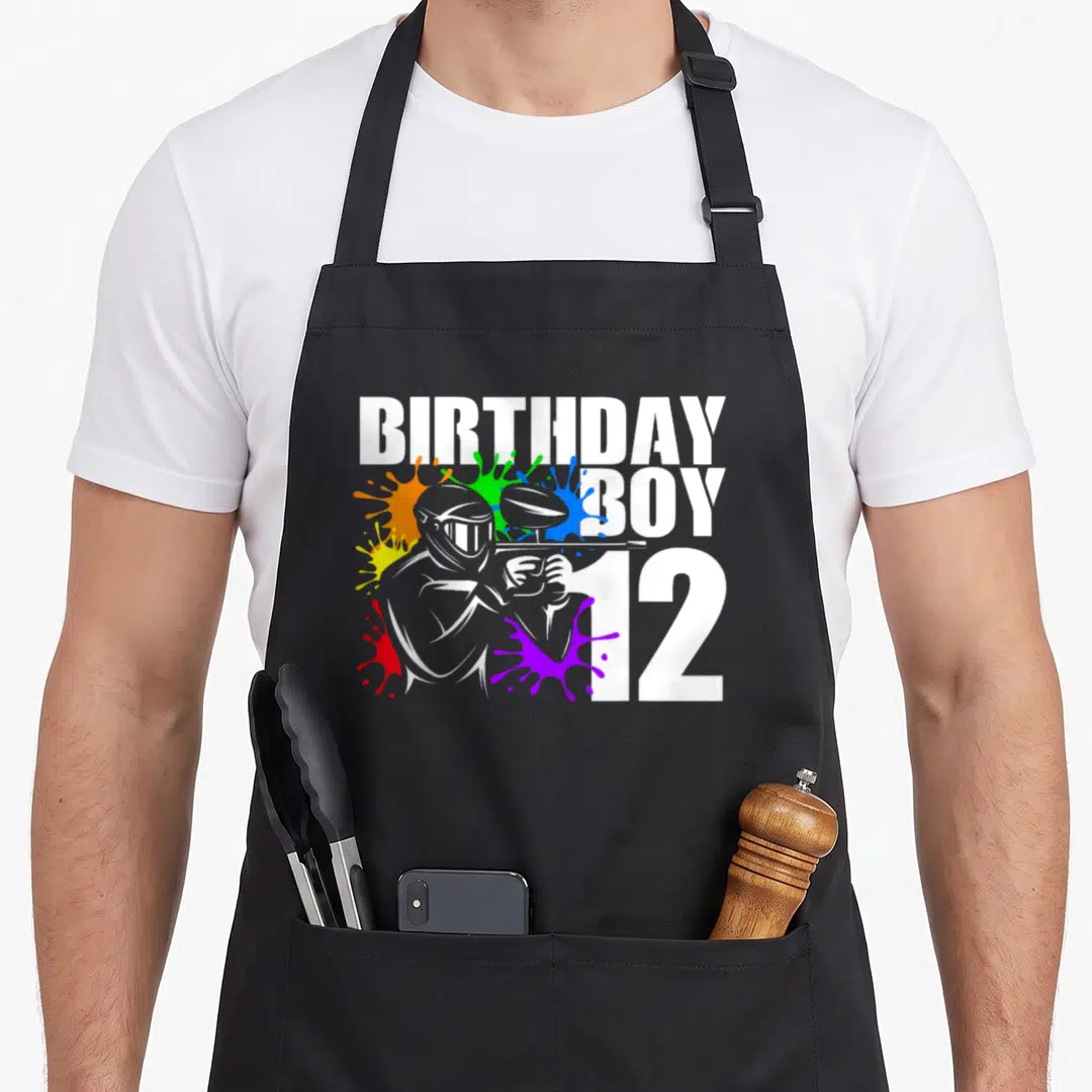 Paintball 12th birthday apron - Grey paintball player surrounded by red yellow green blue purple and orange paint — shown on a black cotton canvas apron against a white background