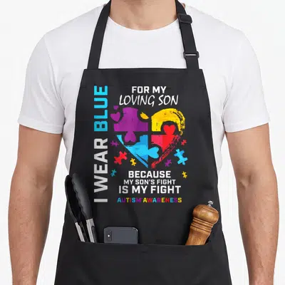 Puzzle dad and son aprons - Multi-colored puzzle heart with I Wear Blue text and Autism Awareness slogan — shown on a black cotton canvas apron against a white background