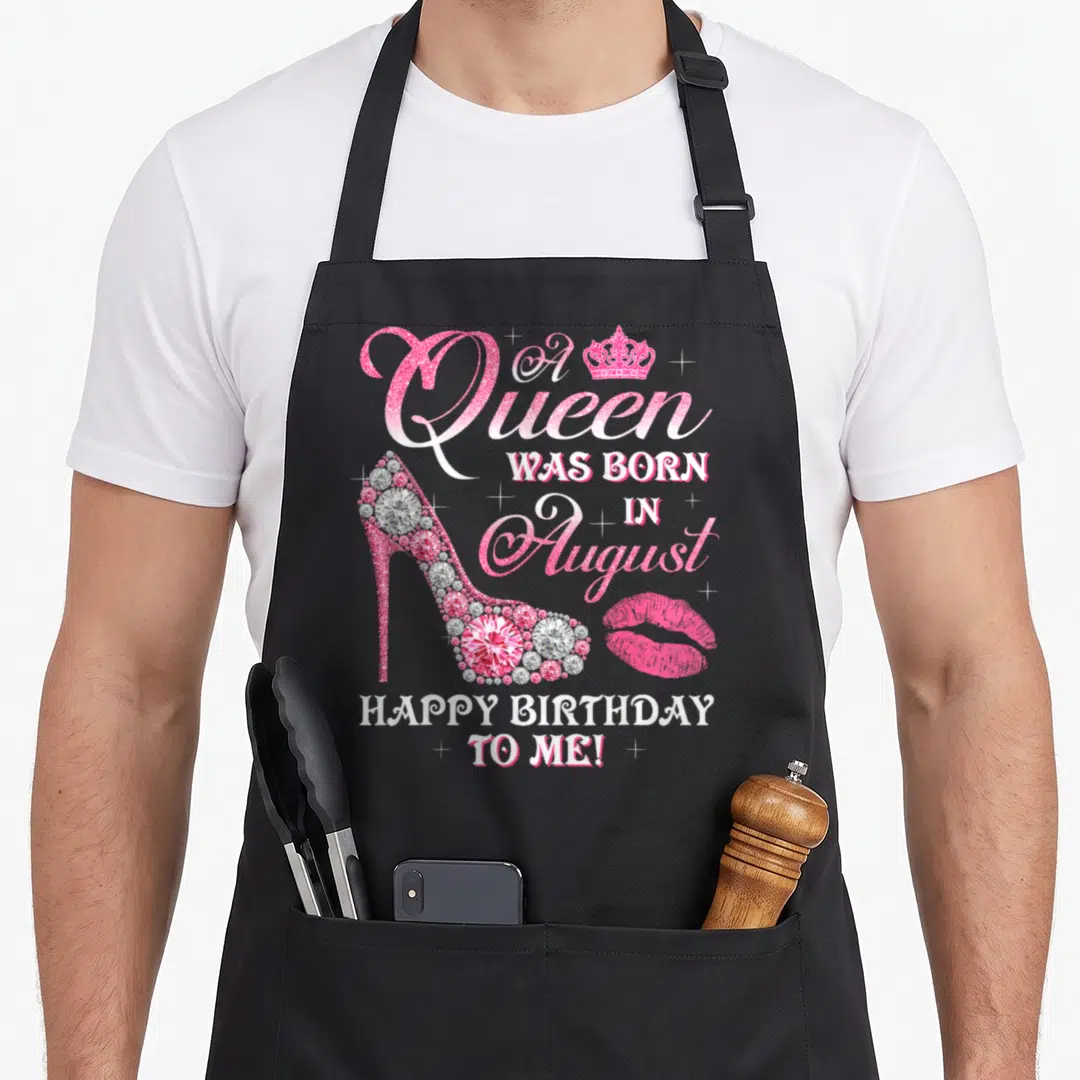 Congratulation queen apron - Pink high heel with diamonds, crown, lips, and A Queen Was Born in August text — shown on a black cotton canvas apron against a white background