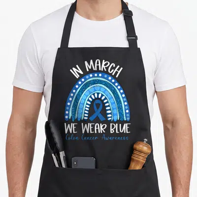 March rainbow apron - Blue rainbow with awareness ribbon and text In March We Wear Blue Colon Cancer Awareness — shown on a black cotton canvas apron against a white background