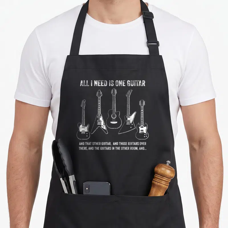 Collection novelty apron - Five white distressed guitars arranged in a row with humorous text about collecting — shown on a black cotton canvas apron against a white background