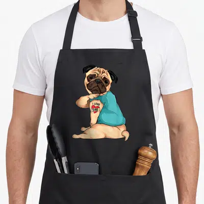 Pug tattoo aprons - Cartoon pug pulling blue shirt to reveal red heart tattoo with I LOVE DAD text — shown on a black cotton canvas apron against a white background