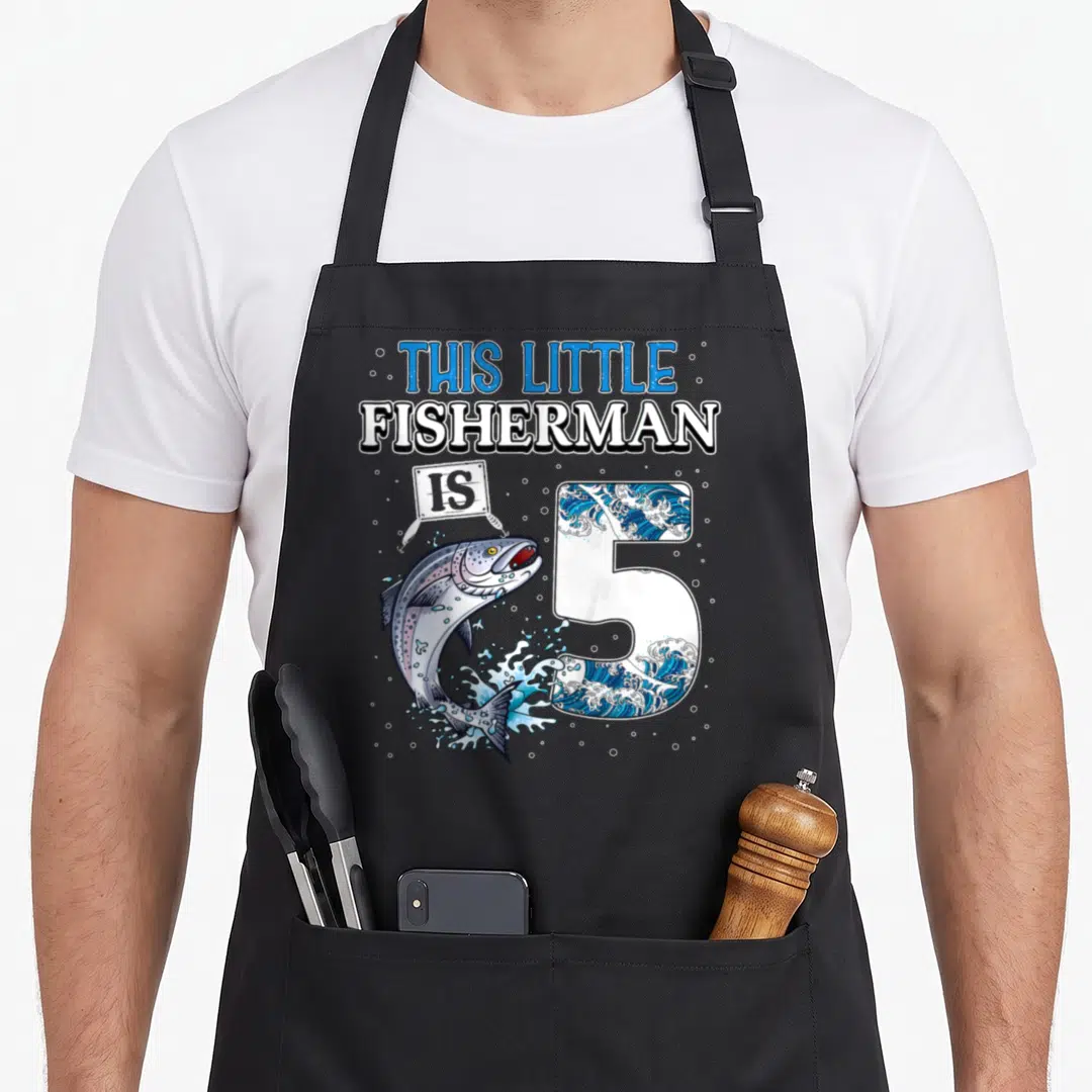 5th fishing aprons - This Little Fisherman is 5 text with jumping fish and wave-filled number 5 — shown on a black cotton canvas apron against a white background