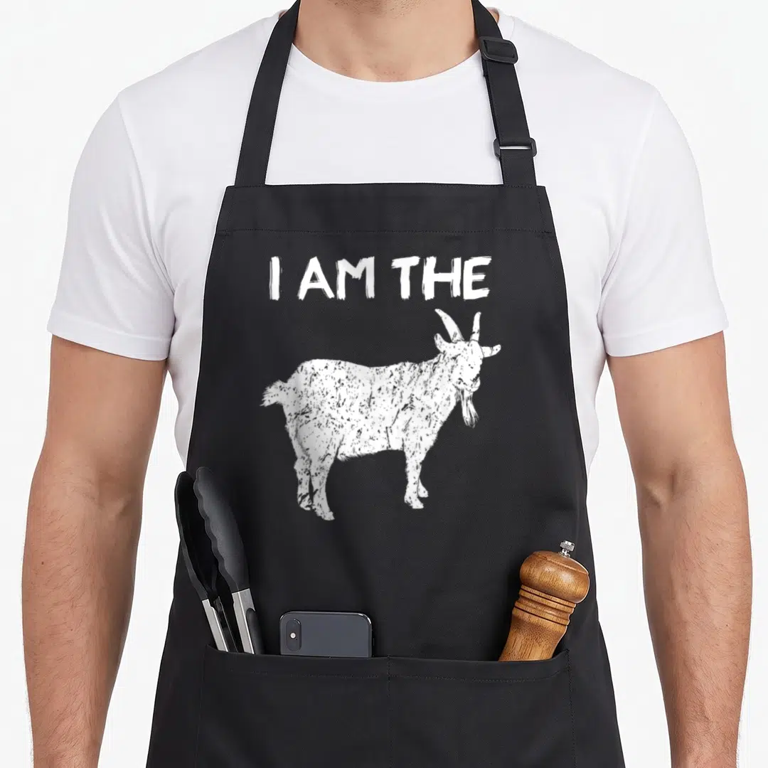 Motivational goat apron - White distressed text I AM THE above a standing goat silhouette — shown on a black cotton canvas apron against a white background