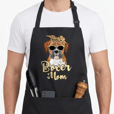 Whisperer boxer dog apron - Cartoon boxer dog with leopard headband and sunglasses, Boxer Mom script text — shown on a black cotton canvas apron against a white background