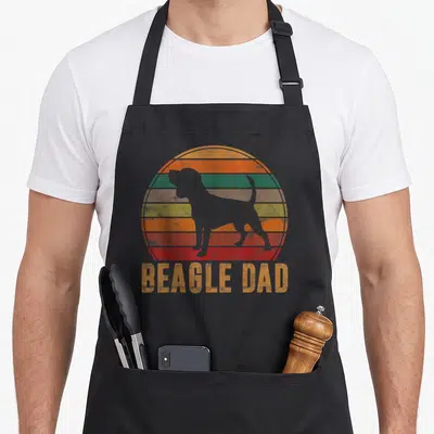 Beagle owner dog apron - Grey beagle silhouette inside a striped orange red yellow green and grey retro sun with beagle — shown on a black cotton canvas apron against a white background
