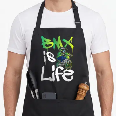 Bmx road apron - BMX IS Life graffiti text with cartoon rider in green and blue — shown on a black cotton canvas apron against a white background