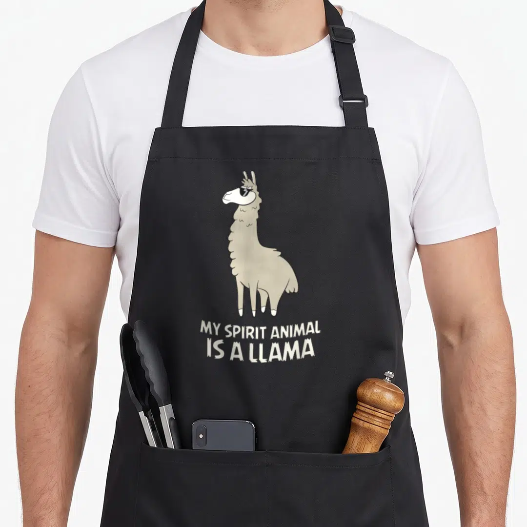 Llamas animal apron - Cartoon llama standing above two lines of stacked white text on grey background — shown on a black cotton canvas apron against a white background
