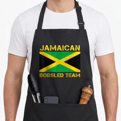 Sled bobsled apron - Jamaica flag with yellow green black X and text JAMAICAN BOBSLED TEAM distressed — shown on a black cotton canvas apron against a white background