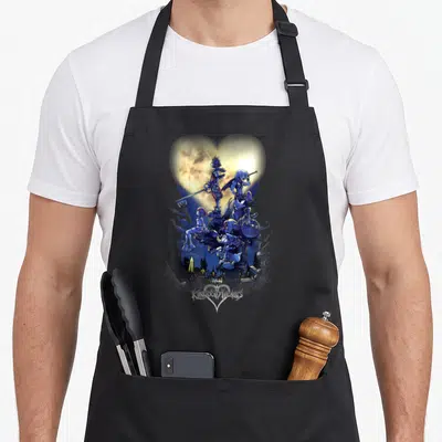 Retro shot apron - Vertical stack of characters inside a glowing heart with KINGDOM HEARTS text at bottom — shown on a black cotton canvas apron against a white background