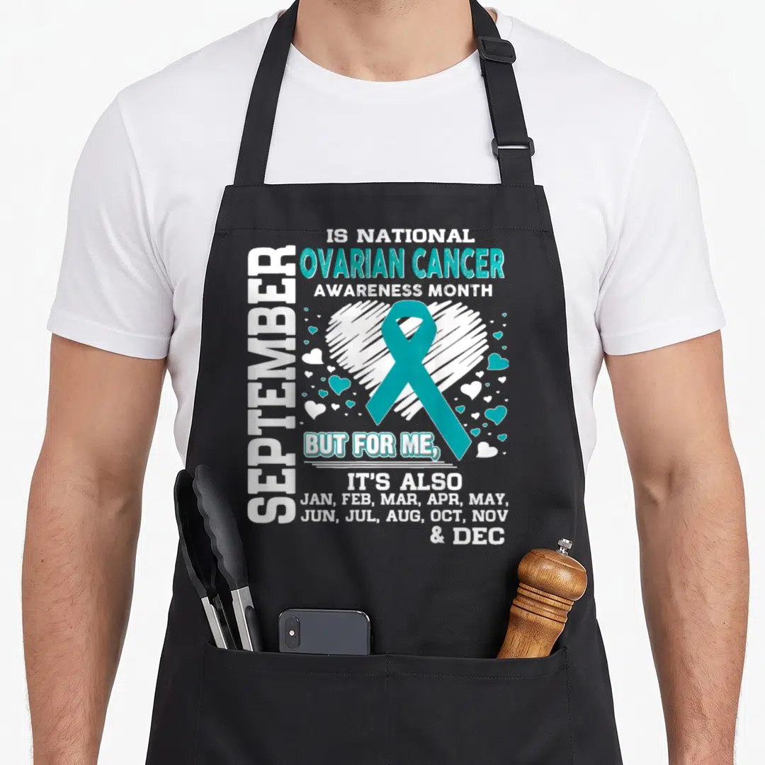 September cancer awareness apron - Teal ribbon over white sketched heart with text listing all twelve months of the year — shown on a black cotton canvas apron against a white background