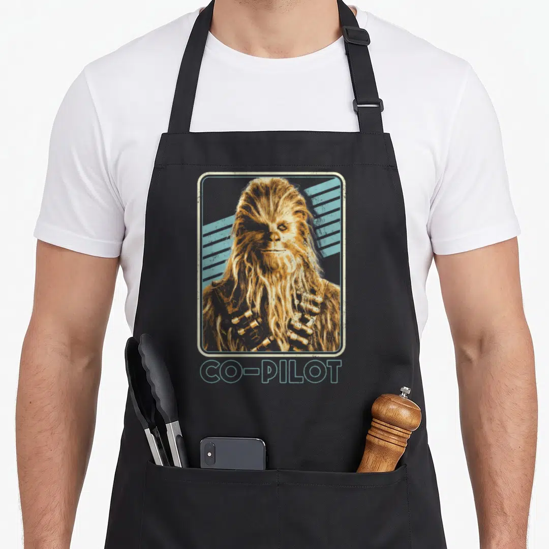 Movie chewie chef and co aprons - Retro Chewbacca portrait in rounded frame with diagonal blue stripes and co-pilot — shown on a black cotton canvas apron against a white background
