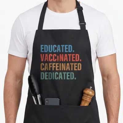 Educated nurse apron - Stacked text reading Educated Vaccinated Caffeinated Dedicated with syringe icon in blue red — shown on a black cotton canvas apron against a white background