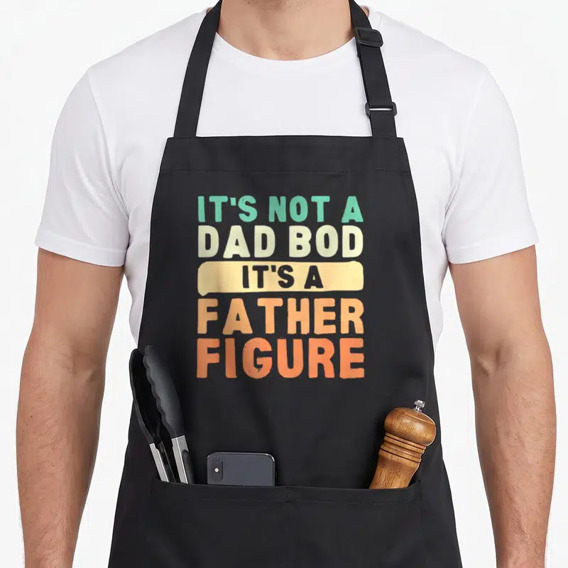 Figure father day apron - Stacked teal beige and orange text reading It's Not A Dad Bod It's A Father Figure — shown on a black cotton canvas apron against a white background