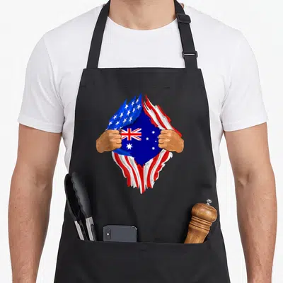 Blood australian apron - Two brown hands rip a USA flag to show Australian flag in blue red white — shown on a black cotton canvas apron against a white background