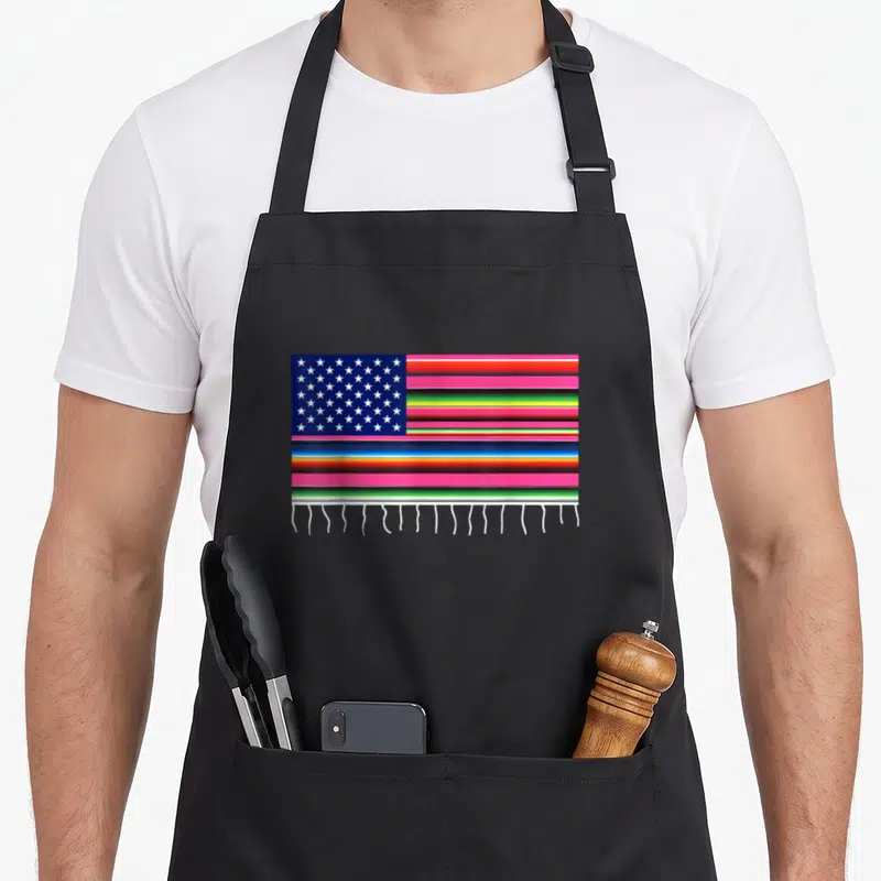 Serape american flag apron - Rectangular flag with blue star field, multicolored stripes, and white fringe — shown on a black cotton canvas apron against a white background