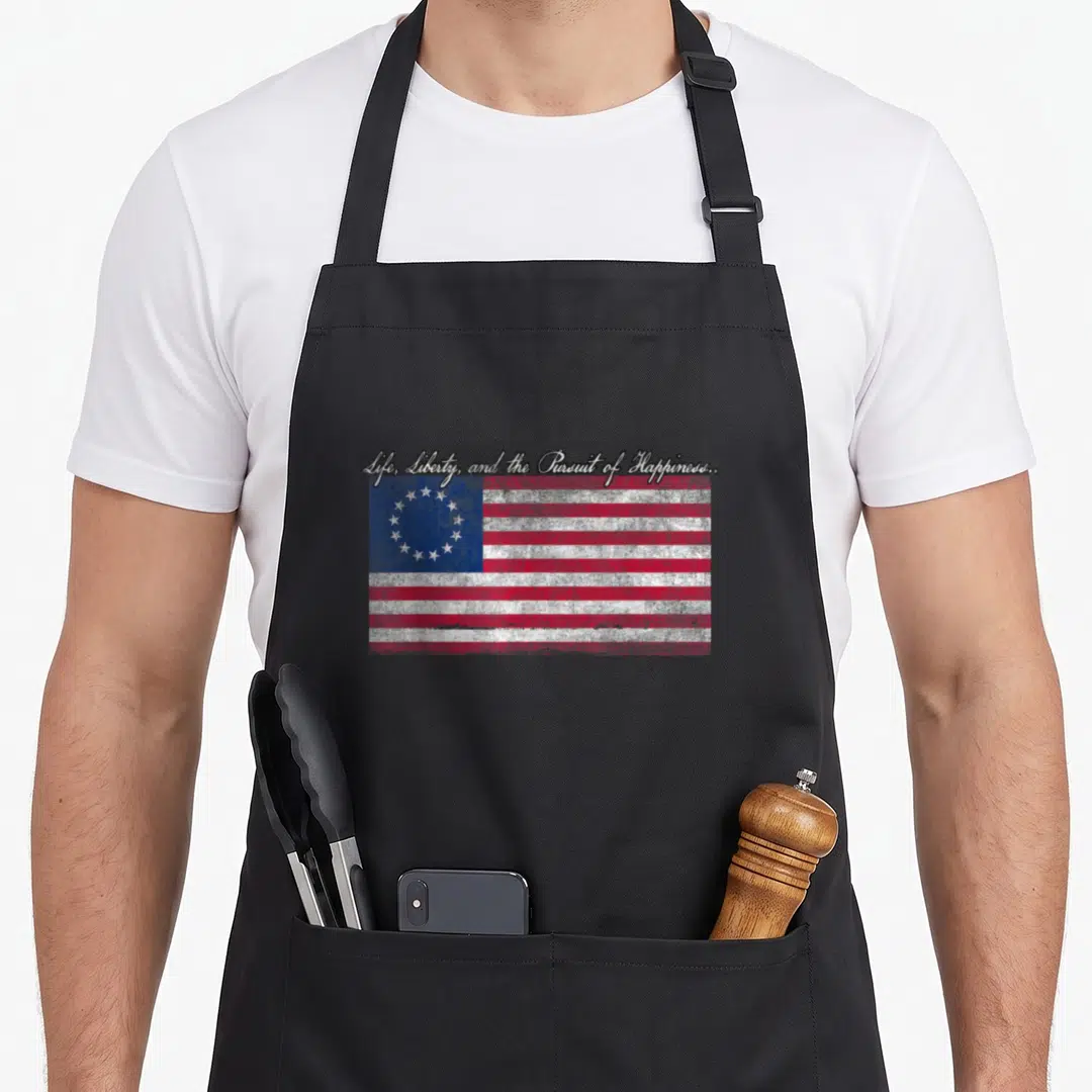 Pursuit liberty apron - Distressed Betsy Ross flag with circular stars and script text reading Life Liberty Pursuit — shown on a black cotton canvas apron against a white background