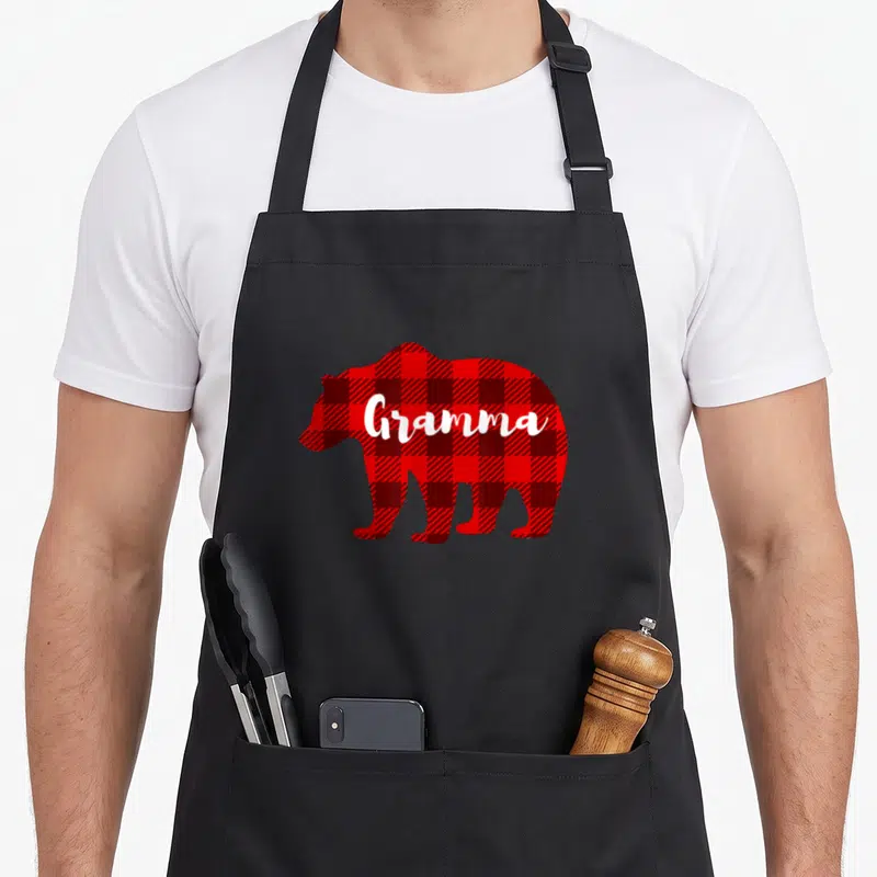 Gramma bear apron - Red and black plaid bear silhouette with white Gramma script text — shown on a black cotton canvas apron against a white background