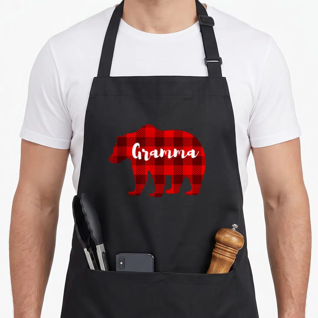 Gramma bear apron - Red and black plaid bear silhouette with white Gramma script text — shown on a black cotton canvas apron against a white background