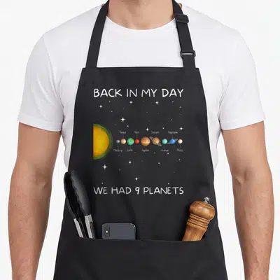 Nine space planets apron - Cartoon solar system with nine planets and Back in My Day text — shown on a black cotton canvas apron against a white background