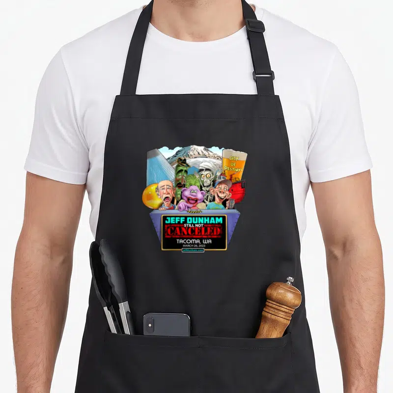 Jeff tacoma apron - Cartoon puppets behind grey barrier reading Jeff Dunham Still Not Canceled Tacoma WA March 26 2023 — shown on a black cotton canvas apron against a white background