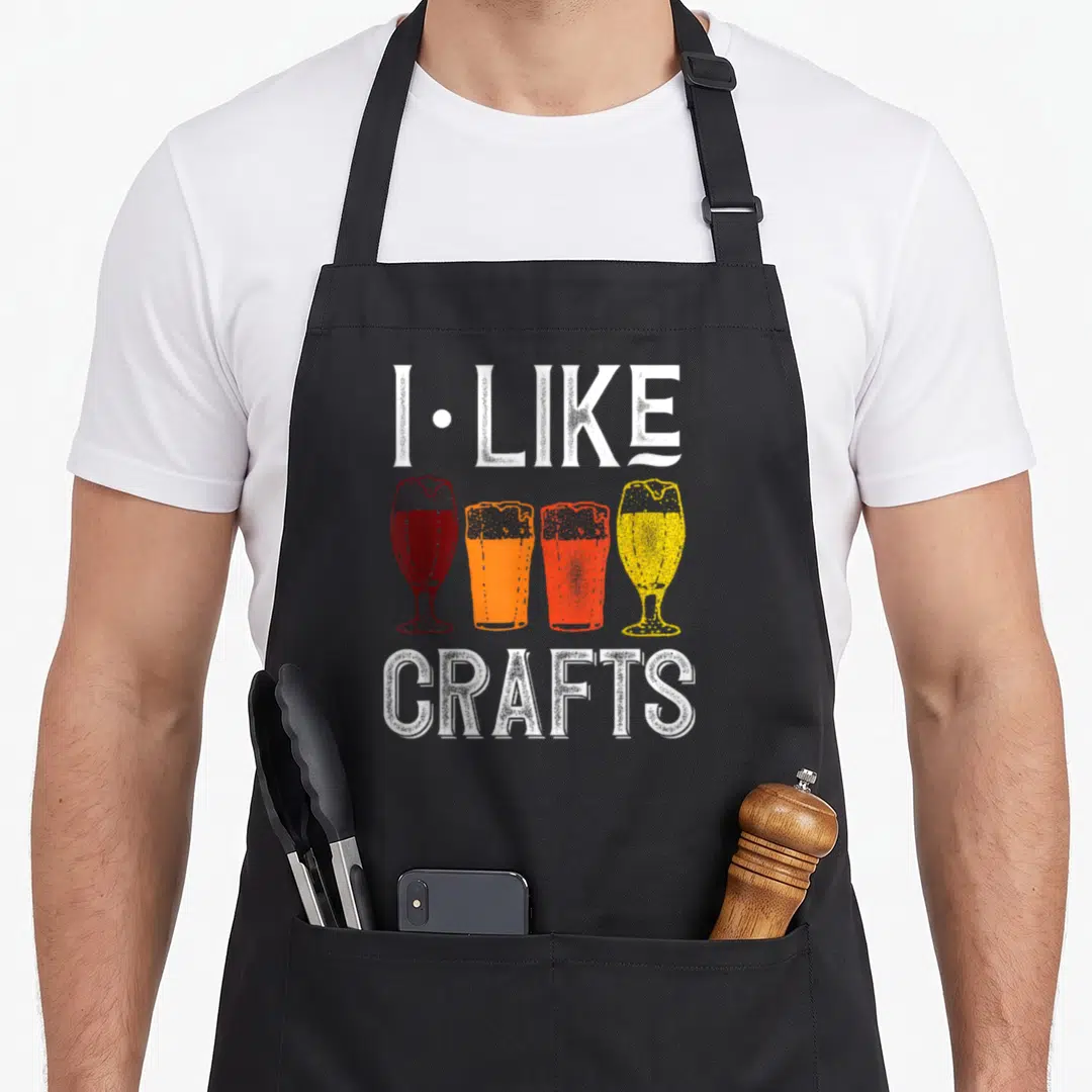 Brewer beer craft apron - I LIKE CRAFTS text with four red orange yellow and white beer glasses in distressed style — shown on a black cotton canvas apron against a white background