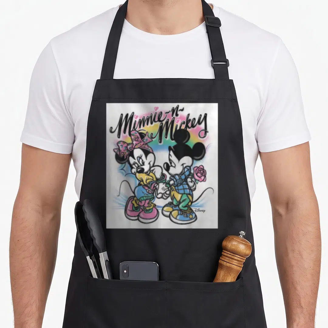 Cute colorful aprons - Minnie-N-Mickey text over cartoon mice holding hands with rainbow and hearts in black pink blue — shown on a black cotton canvas apron against a white background