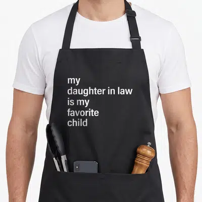 Law father mom and daughter aprons - white text reading my daughter in law is my favorite child on black fabric — shown on a black cotton canvas apron against a white background