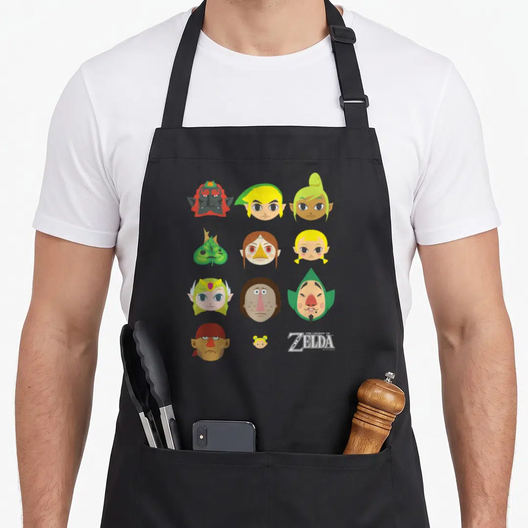 Simple character aprons - Twelve character heads in a grid with The Legend of Zelda logo in white, green, red — shown on a black cotton canvas apron against a white background
