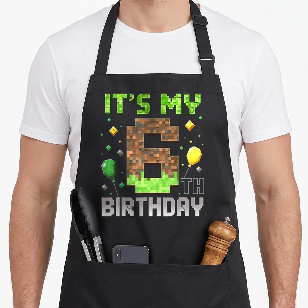 6th birthday video game apron - Pixelated number 6 with dirt texture, gem balloons, and IT'S MY 6 TH BIRTHDAY text — shown on a black cotton canvas apron against a white background