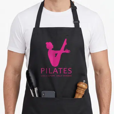 Pilate gag aprons - Pink female silhouette stretching above centered text reading PILATES LIKE A SPORT ONLY HARDER — shown on a black cotton canvas apron against a white background