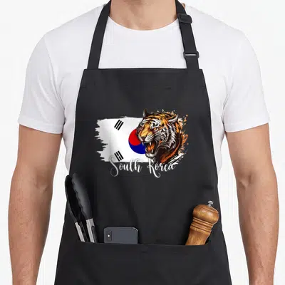 Youth korean apron - Realistic tiger head over white blue red black flag with South Korea script text — shown on a black cotton canvas apron against a white background