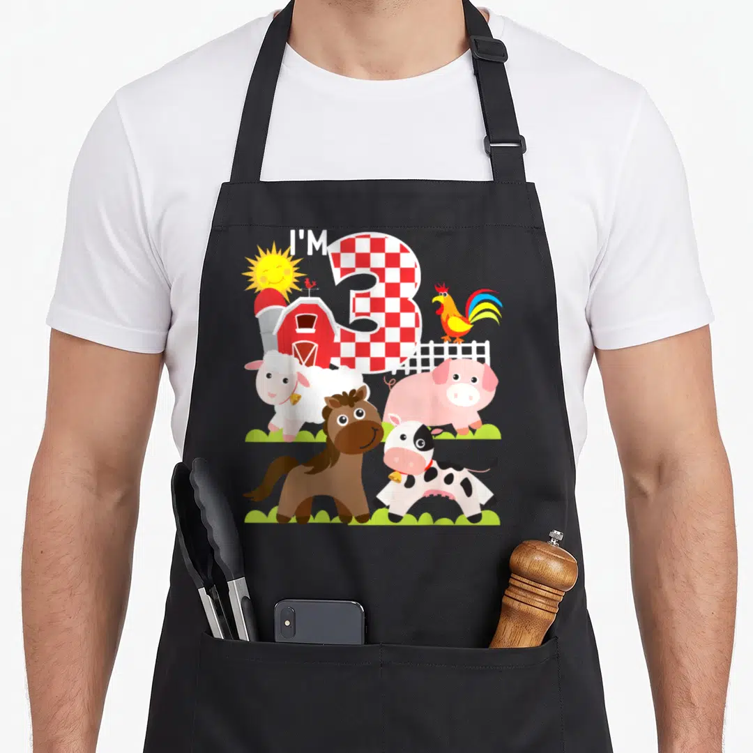 Barnyard farm apron - I'M 3 text with checkered number, barn, rooster, cow, pig, horse, sheep, sun — shown on a black cotton canvas apron against a white background