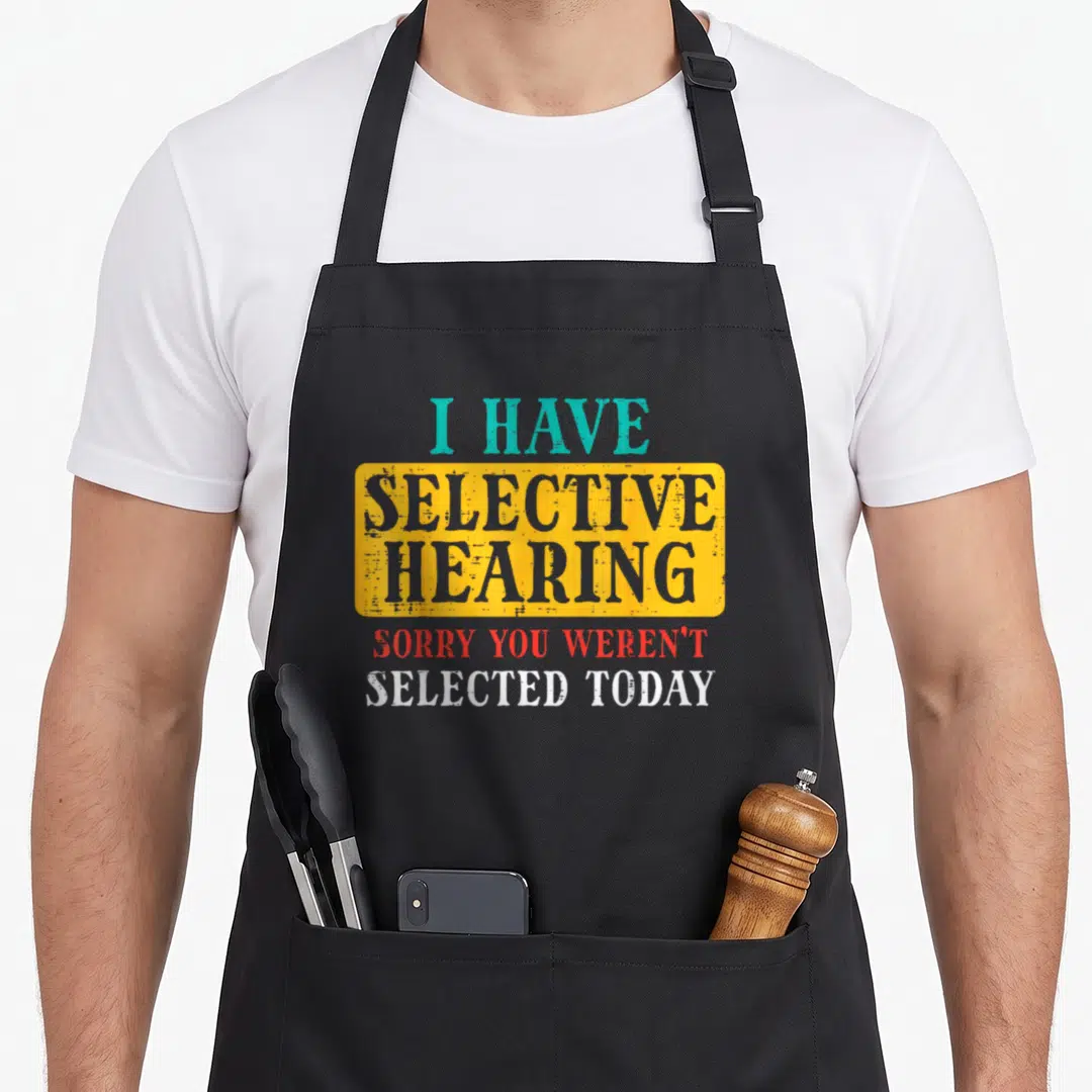Selective humorous aprons - I HAVE SELECTIVE HEARING text inside yellow rectangle with red and white bottom lines — shown on a black cotton canvas apron against a white background