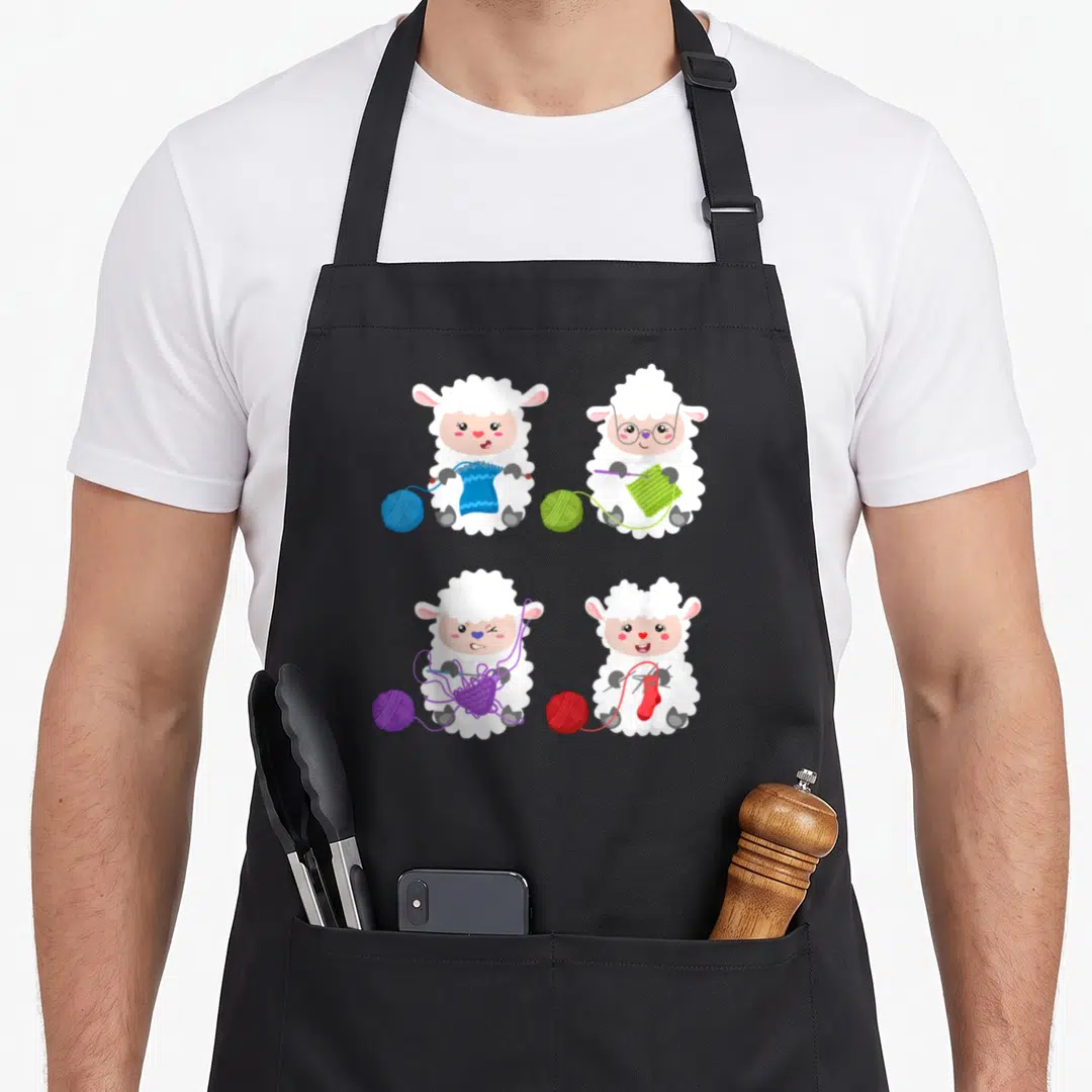 Knit crochet apron - Four cartoon sheep knitting and crocheting with blue, green, purple, and red yarn balls — shown on a black cotton canvas apron against a white background