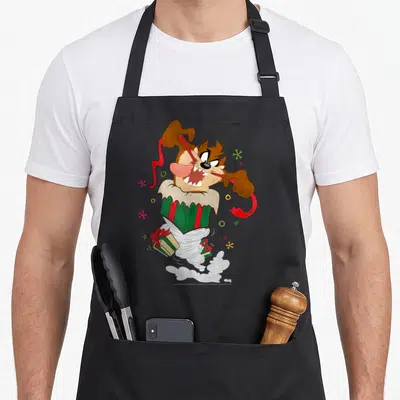 Taz christmas apron - Cartoon Tasmanian Devil in striped tornado holding red ribbon with gift boxes and snowflakes — shown on a black cotton canvas apron against a white background