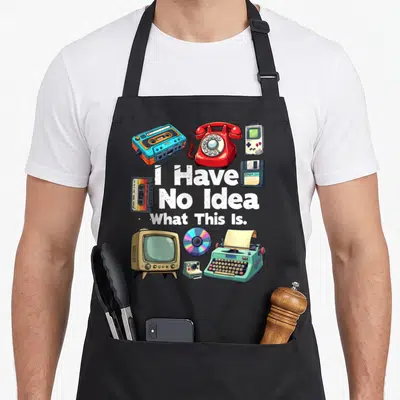 Funny bro 80s apron - I Have No Idea What This Is text surrounded by retro cassette, phone, tv, and typewriter — shown on a black cotton canvas apron against a white background